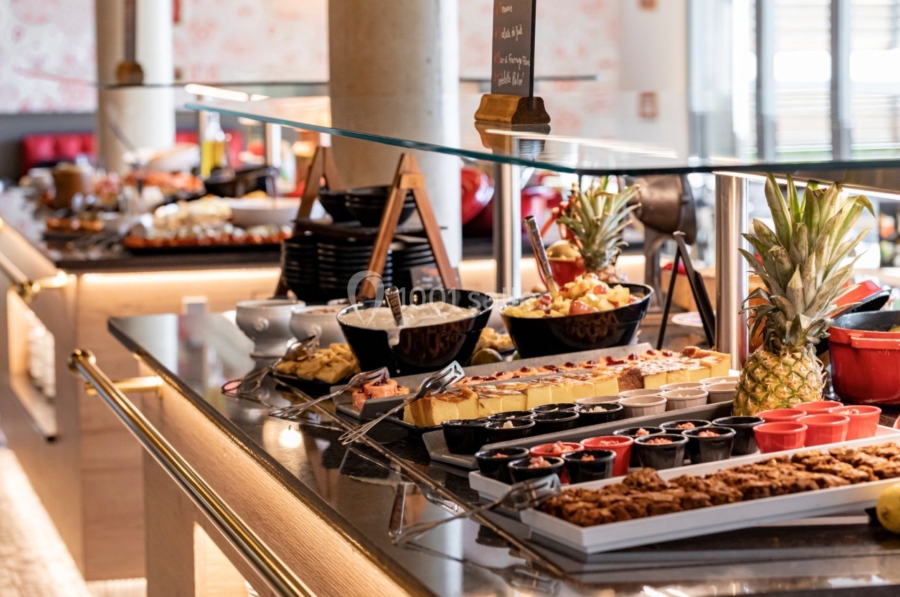 Buffet varié avec desserts, fruits frais, plats salés et boissons disposés sur un comptoir en verre.
