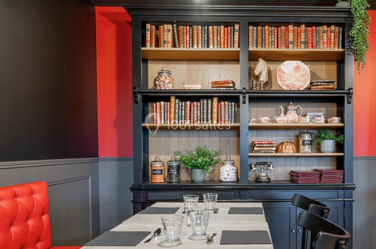 Bibliothèque en bois noir avec livres anciens, objets décoratifs et plantes, située derrière une table dressée.