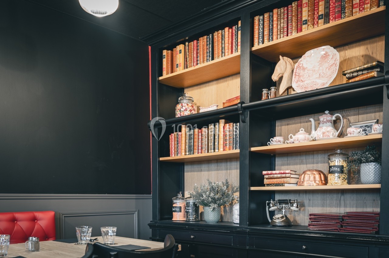 Bibliothèque en bois noir avec livres anciens, objets décoratifs et vaisselle, dans une pièce au style vintage.