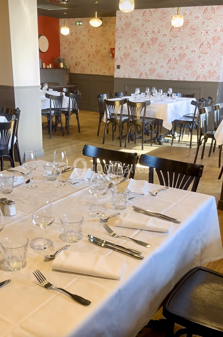 Salle de restaurant lumineuse avec tables dressées, nappes blanches, verres et couverts, décor mural à motifs floraux.