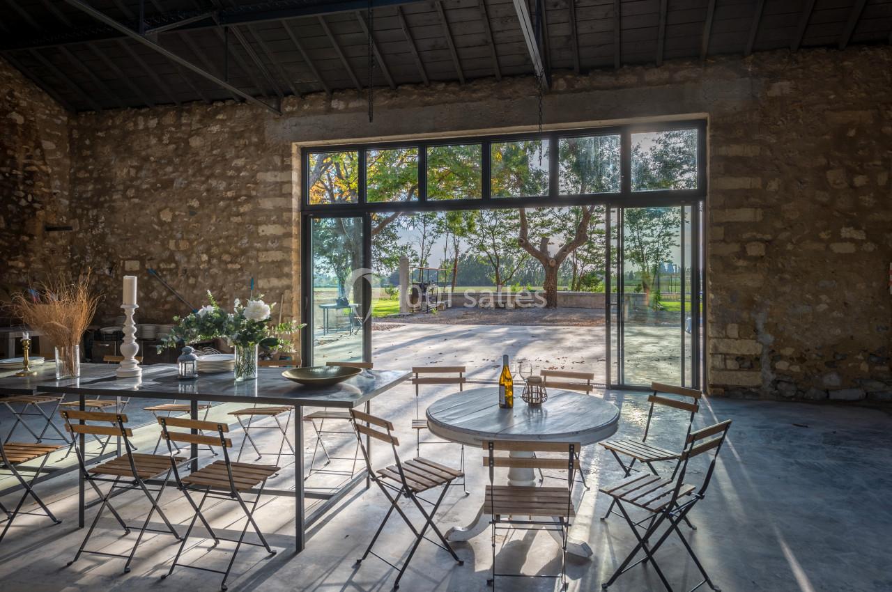 Salle lumineuse avec des murs en pierre, tables et chaises en bois, donnant sur un espace extérieur arboré.