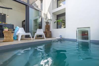 Chambre lumineuse avec lit double, fauteuil beige, fenêtre ouverte sur un paysage et décoration murale en osier.