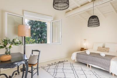 Chambre lumineuse avec lit double, fauteuil beige, fenêtre ouverte sur un paysage et décoration murale en osier.