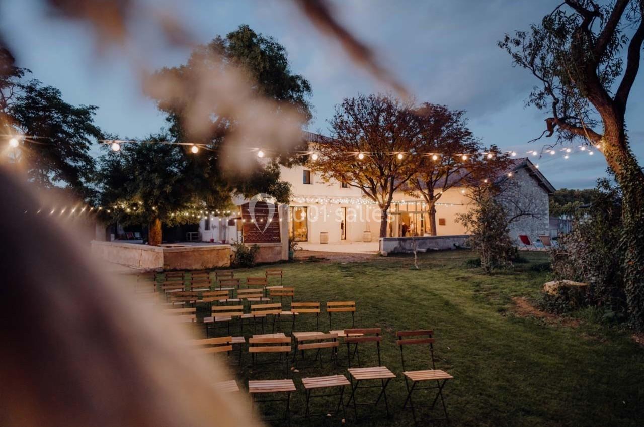 Chaises disposées en extérieur devant un bâtiment éclairé, entouré d'arbres et décoré de guirlandes lumineuses.