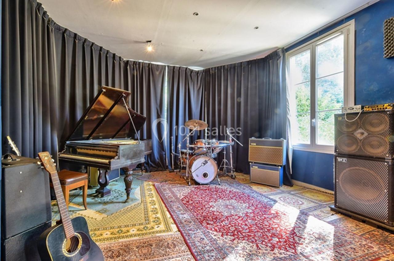 Salle de musique équipée d'un piano à queue, d'une batterie, d'une guitare acoustique et d'amplificateurs, avec tapis au sol.