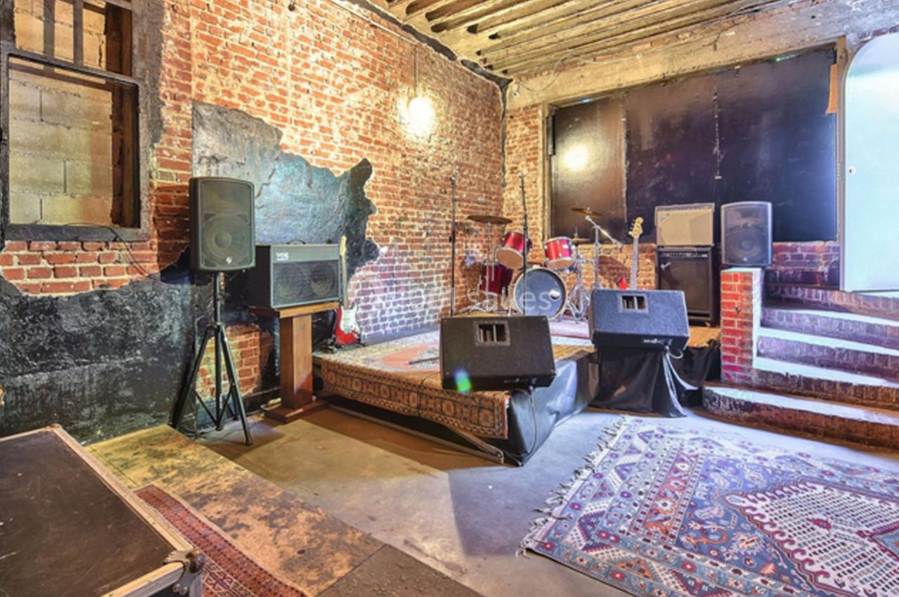 Salle de concert avec murs en briques, scène équipée de batteries, amplificateurs et tapis au sol.