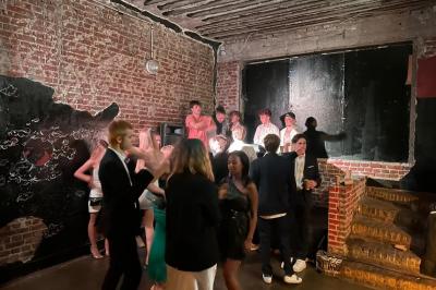 Groupe de personnes discutant et partageant un moment convivial en extérieur, éclairé par une lumière nocturne.