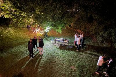 Groupe de personnes discutant et partageant un moment convivial en extérieur, éclairé par une lumière nocturne.