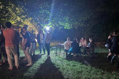 Groupe de personnes discutant et partageant un moment convivial en extérieur, éclairé par une lumière nocturne.