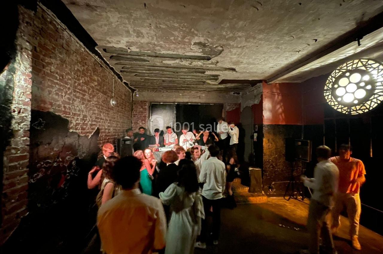 Personnes dansant et discutant dans une salle sombre avec murs en briques et éclairage tamisé.