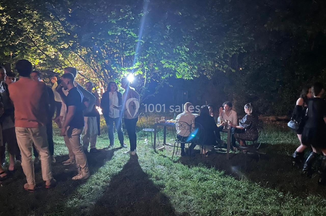 Groupe de personnes discutant et partageant un moment convivial en extérieur, éclairé par une lumière nocturne.