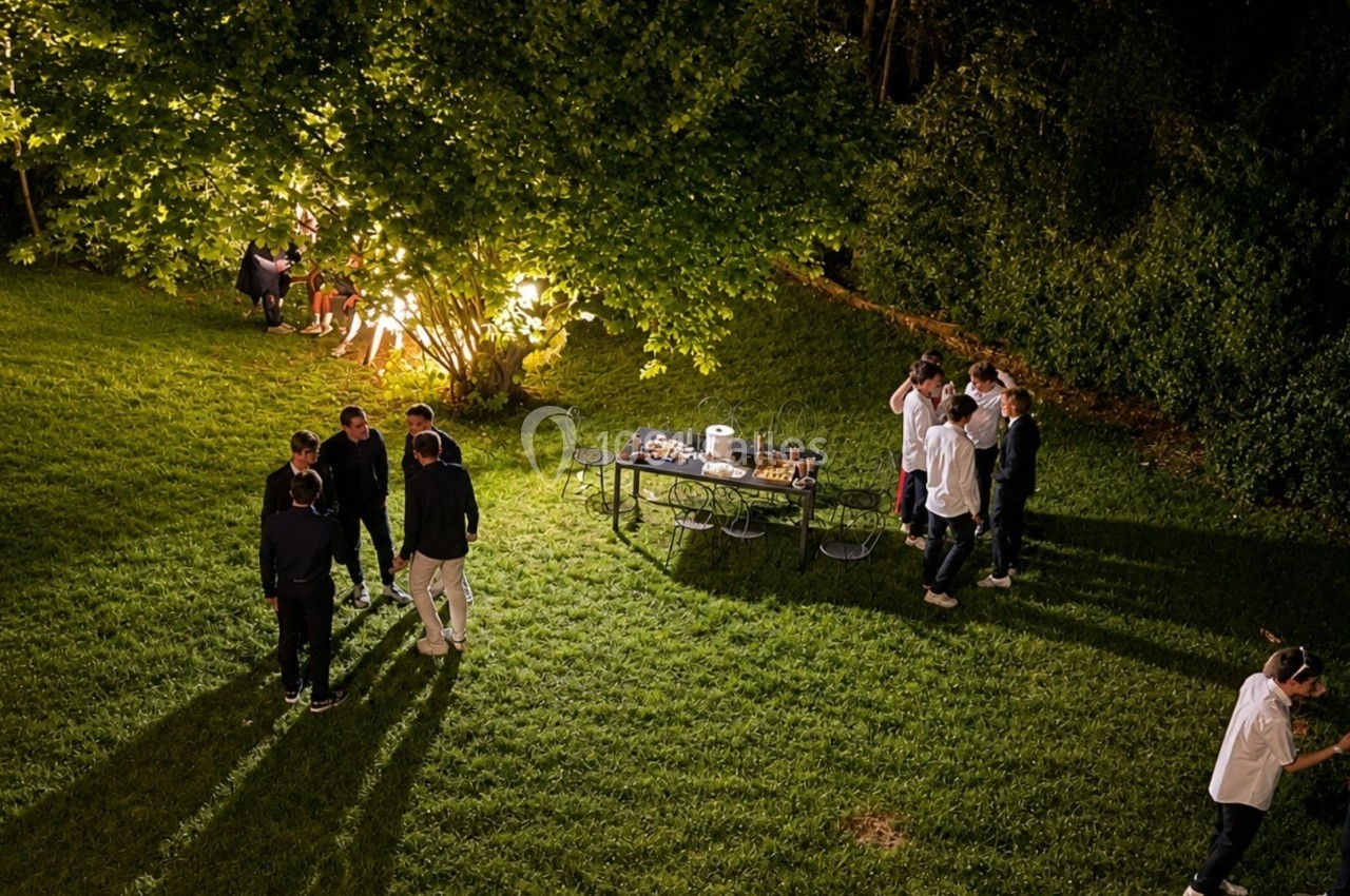 Groupe de personnes discutant et partageant un moment convivial dans un jardin éclairé en soirée.