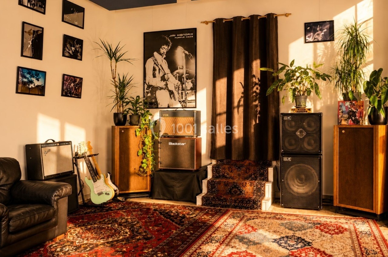 Salle de musique chaleureuse avec amplificateurs, guitares, plantes et photos accrochées aux murs.
