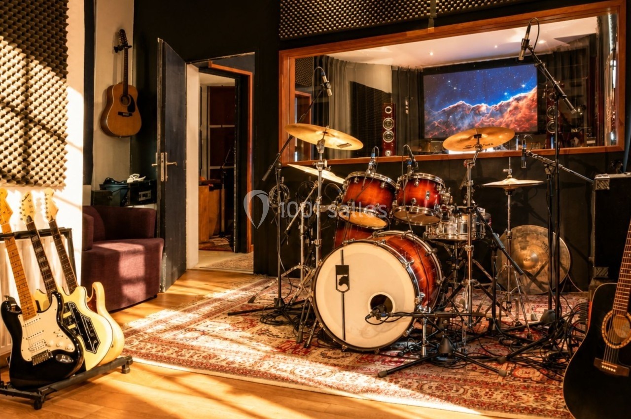 Studio d'enregistrement avec une batterie, des guitares, des amplificateurs et un écran affichant une image spatiale.