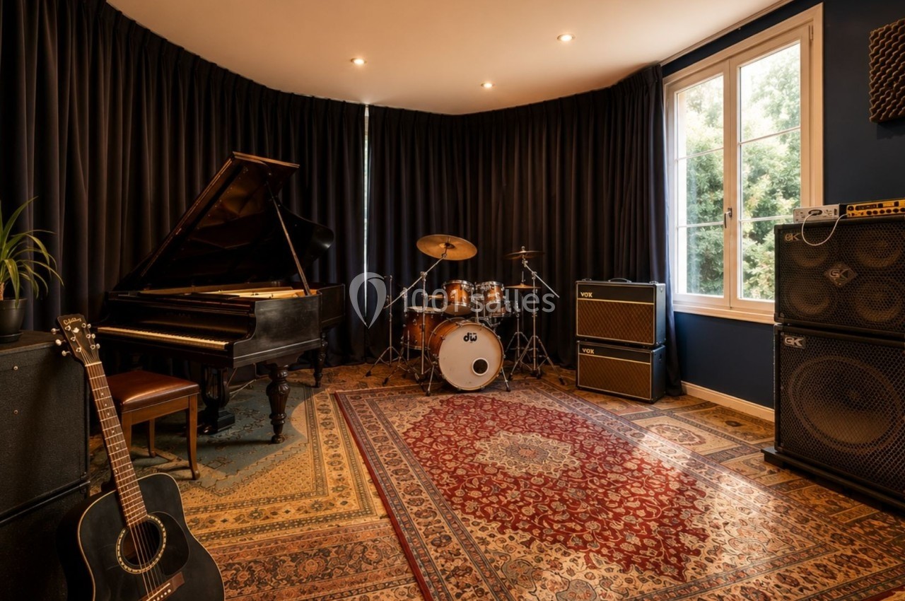 Salle de musique équipée d'un piano à queue, d'une batterie, d'amplificateurs et de guitares, avec tapis et rideaux sombres.