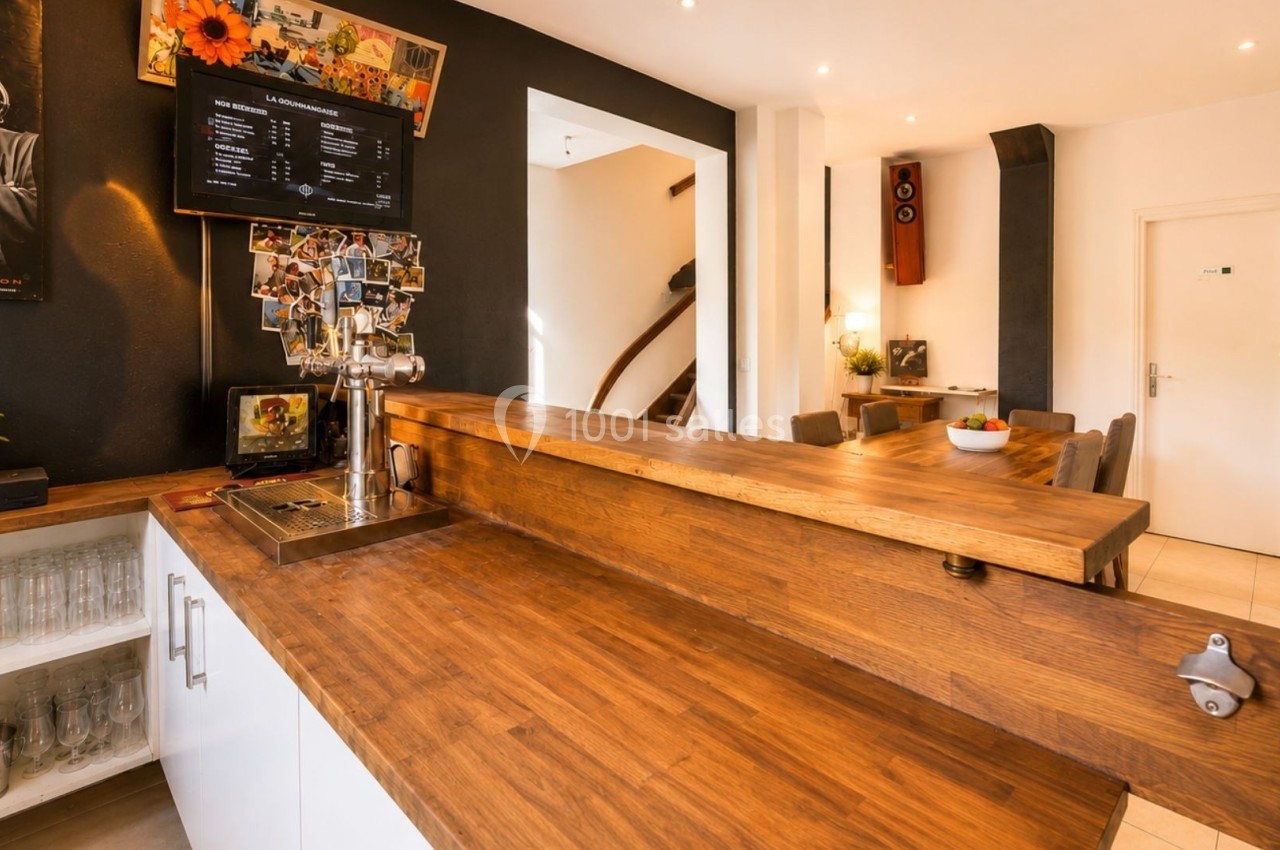 Comptoir en bois dans un intérieur lumineux avec décoration murale, plantes et table à manger en arrière-plan.