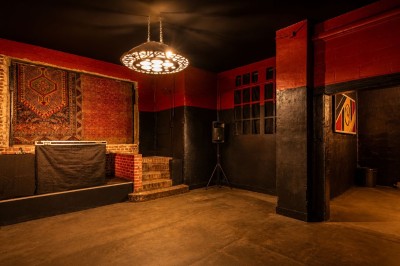Salle sombre avec éclairage rouge et bleu, une estrade avec équipement audio et un tapis mural en arrière-plan.