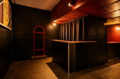 Salle sombre avec éclairage rouge et bleu, une estrade avec équipement audio et un tapis mural en arrière-plan.