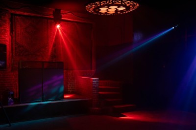 Salle sombre avec éclairage rouge et bleu, une estrade avec équipement audio et un tapis mural en arrière-plan.