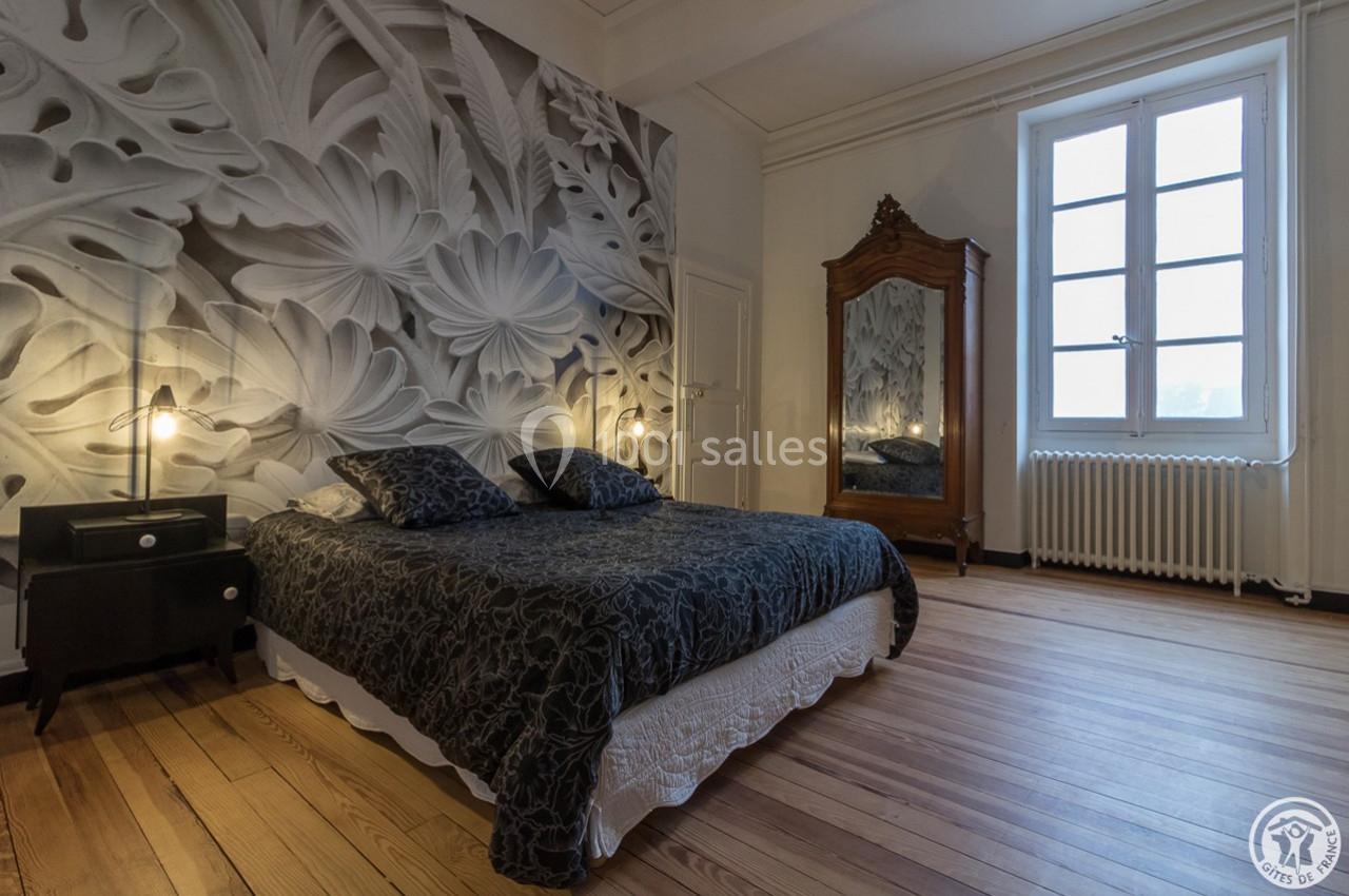 Chambre avec lit double, parquet en bois, armoire ancienne et mur décoré d'une fresque florale en noir et blanc.