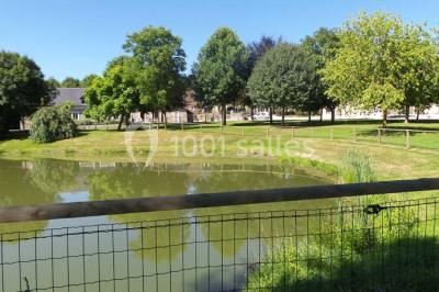 Vue aérienne d'un domaine rural avec bâtiments en pierre, cour centrale, champs, étang et arbres environnants.