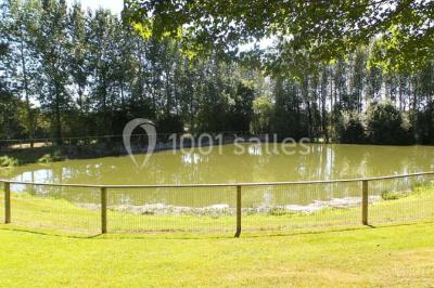 Vue aérienne d'un domaine rural avec bâtiments en pierre, cour centrale, champs, étang et arbres environnants.