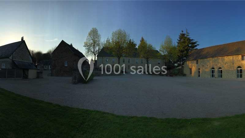 Cour d'une grande propriété avec bâtiments en pierre, arbres en arrière-plan et ciel dégagé au crépuscule.