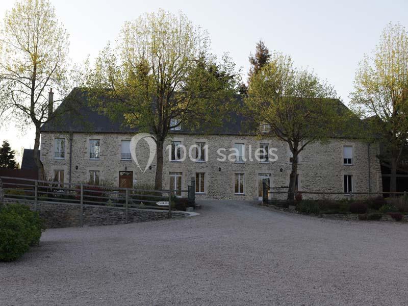 Façade d'une grande maison en pierre entourée d'arbres, avec une allée en gravier au premier plan.