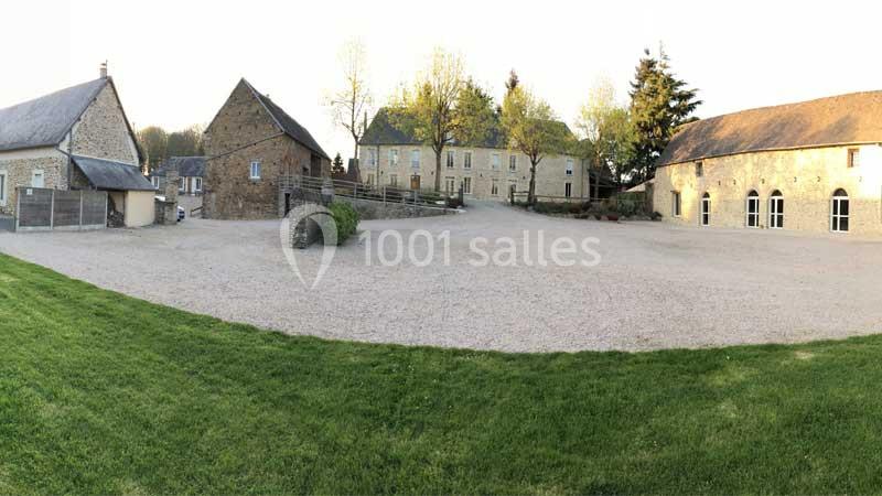 Cour spacieuse entourée de bâtiments en pierre, avec pelouse au premier plan et arbres en arrière-plan.