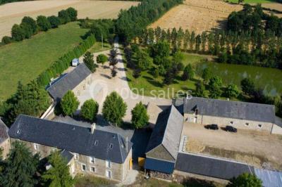 Vue aérienne d'un domaine rural avec bâtiments en pierre, cour centrale, champs, étang et arbres environnants.