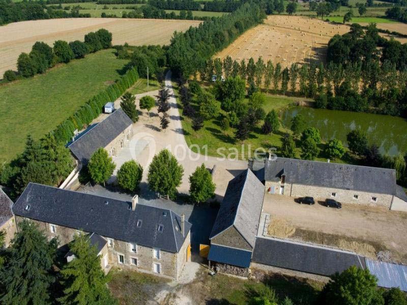 Vue aérienne d'un domaine rural avec bâtiments en pierre, cour centrale, champs, étang et arbres environnants.