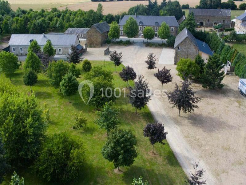 Vue aérienne d'un domaine rural avec bâtiments en pierre, cour centrale et espaces verts arborés.