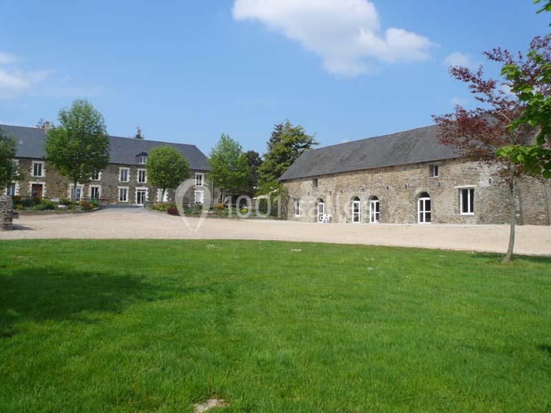Bâtiments en pierre entourés de pelouses et d'arbres sous un ciel bleu avec quelques nuages.