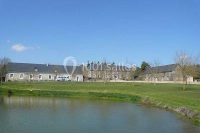 Vue aérienne d'un domaine rural avec bâtiments en pierre, cour centrale, champs, étang et arbres environnants.