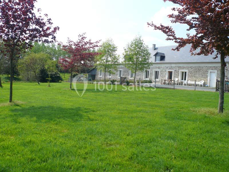 Grande maison en pierre avec terrasse, entourée d'un vaste jardin verdoyant et d'arbres aux feuillages colorés.