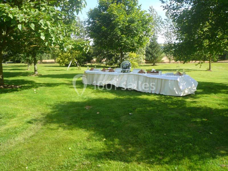 Table dressée avec nappes blanches et plats disposés dans un jardin verdoyant sous des arbres.