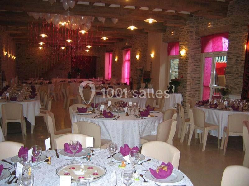 Salle de réception décorée avec des tables rondes dressées, nappes blanches et accents de couleur violette.