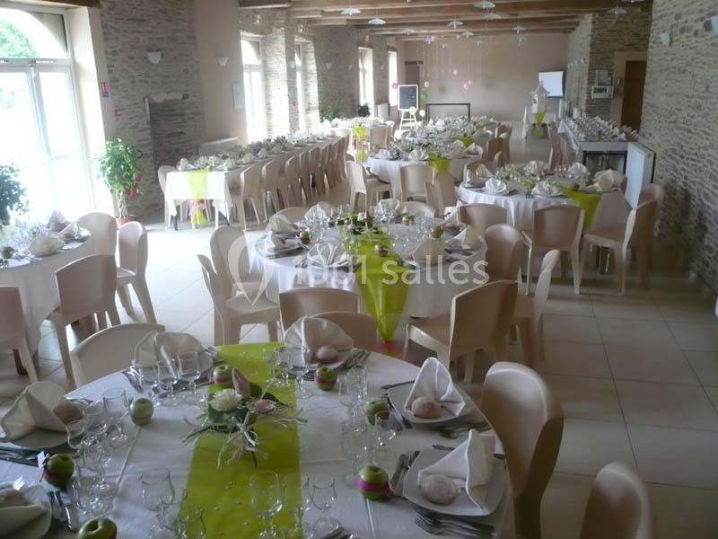 Salle de réception décorée avec des tables rondes, nappes blanches, chemins de table verts et vaisselle dressée.