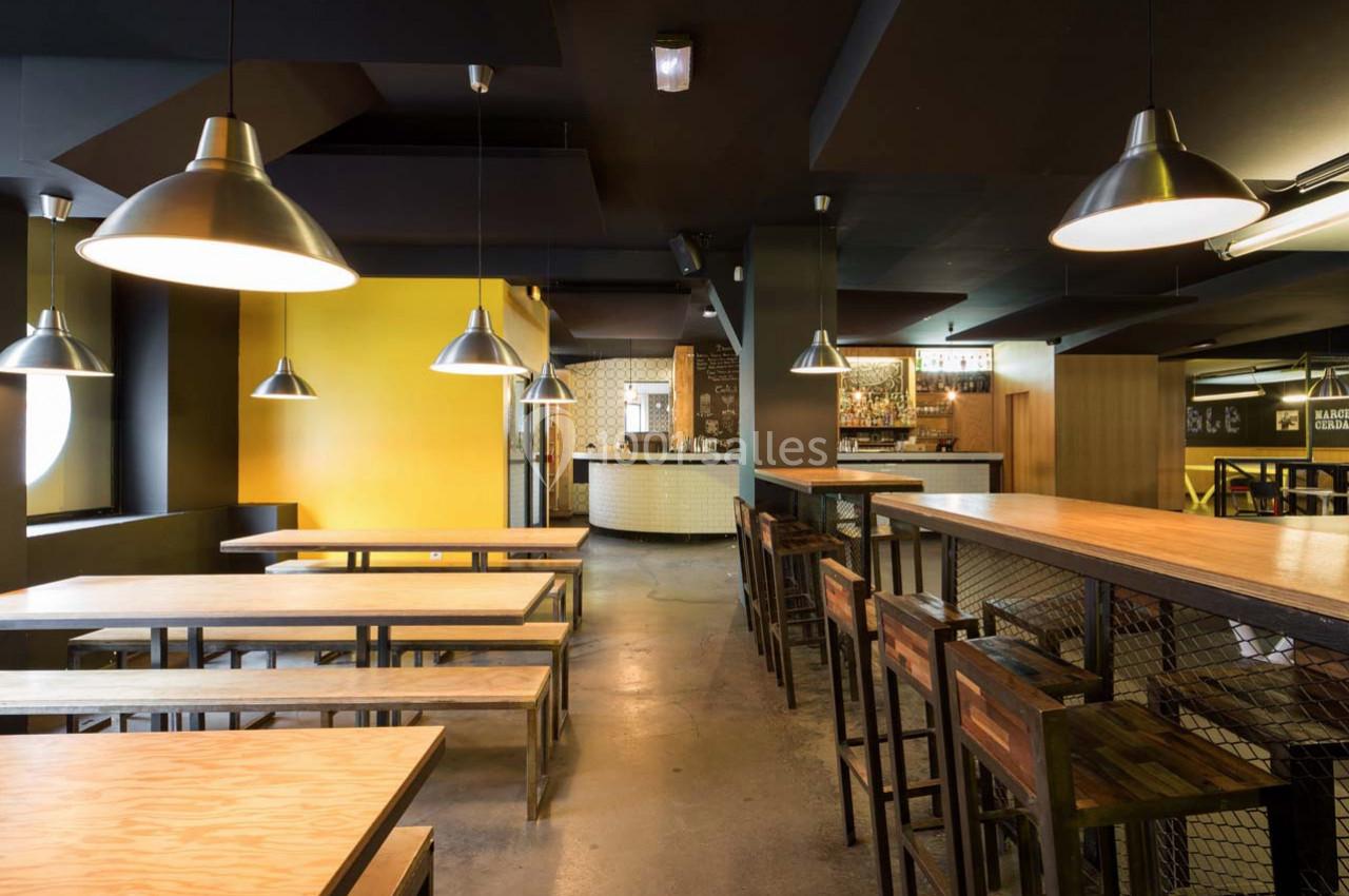 Salle de restaurant moderne avec tables en bois, chaises hautes et éclairage suspendu dans un décor industriel.