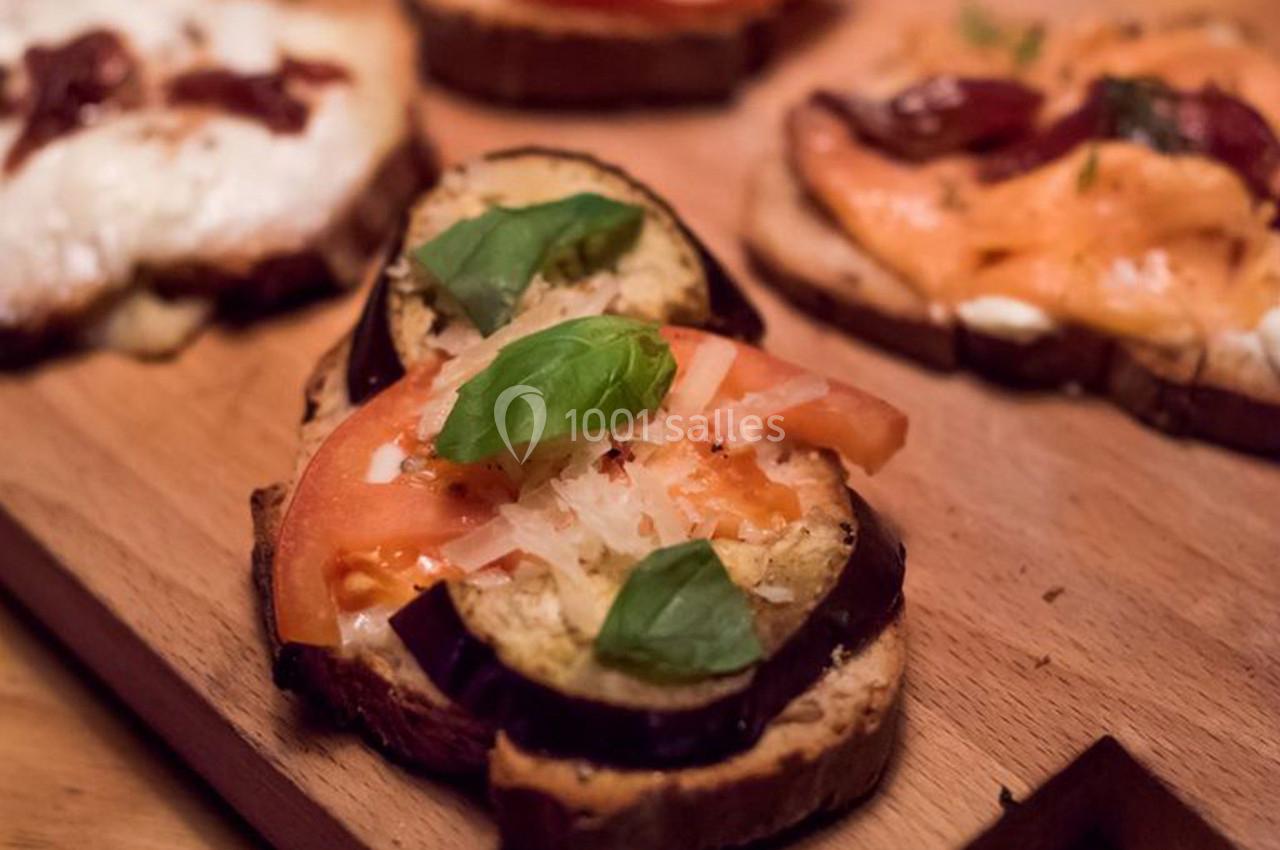 Tranches de pain garnies de légumes grillés, fromage et feuilles de basilic, présentées sur une planche en bois.