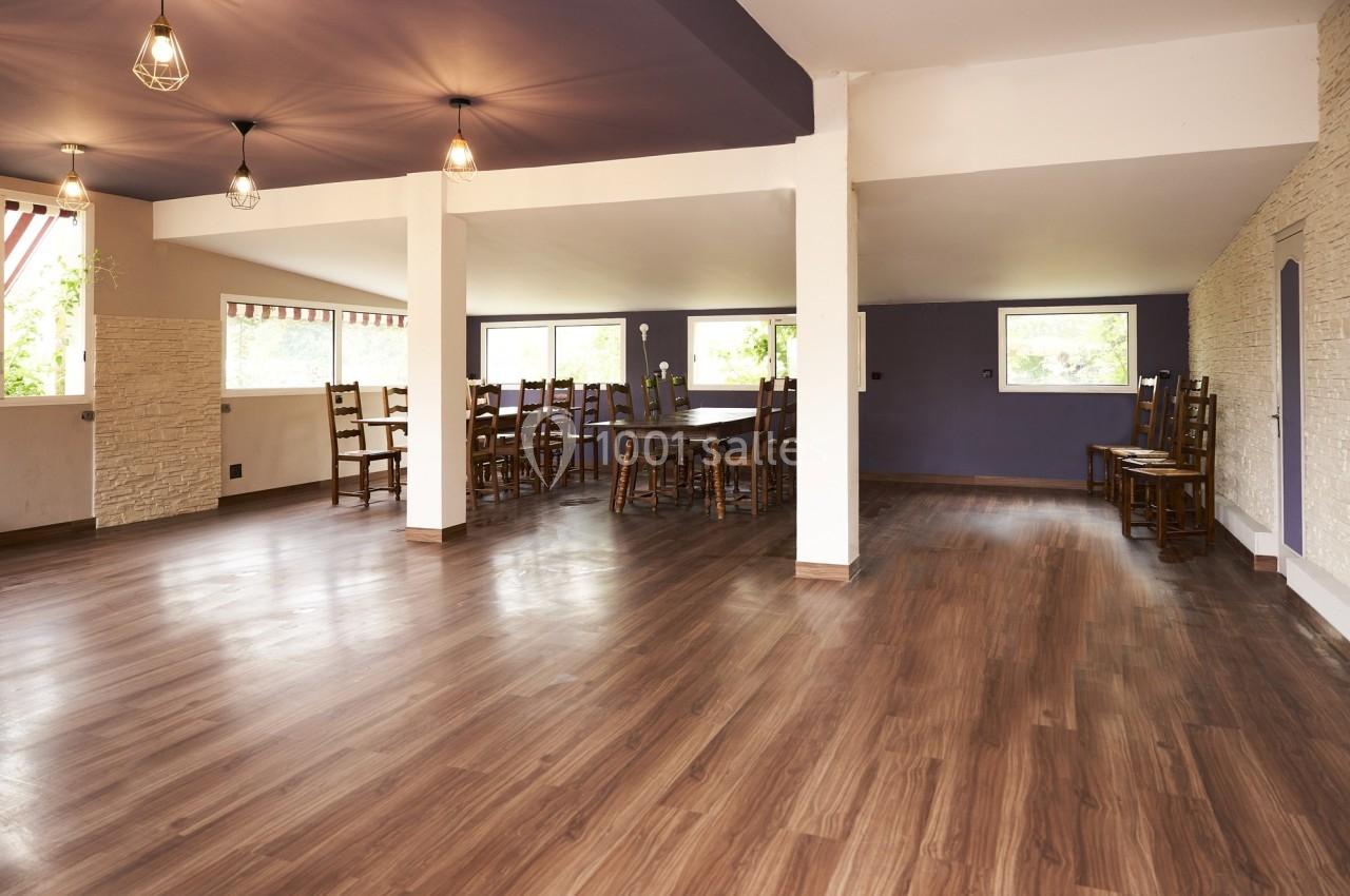 Salle spacieuse avec parquet en bois, murs clairs, plafond violet et grandes fenêtres laissant entrer la lumière naturelle.