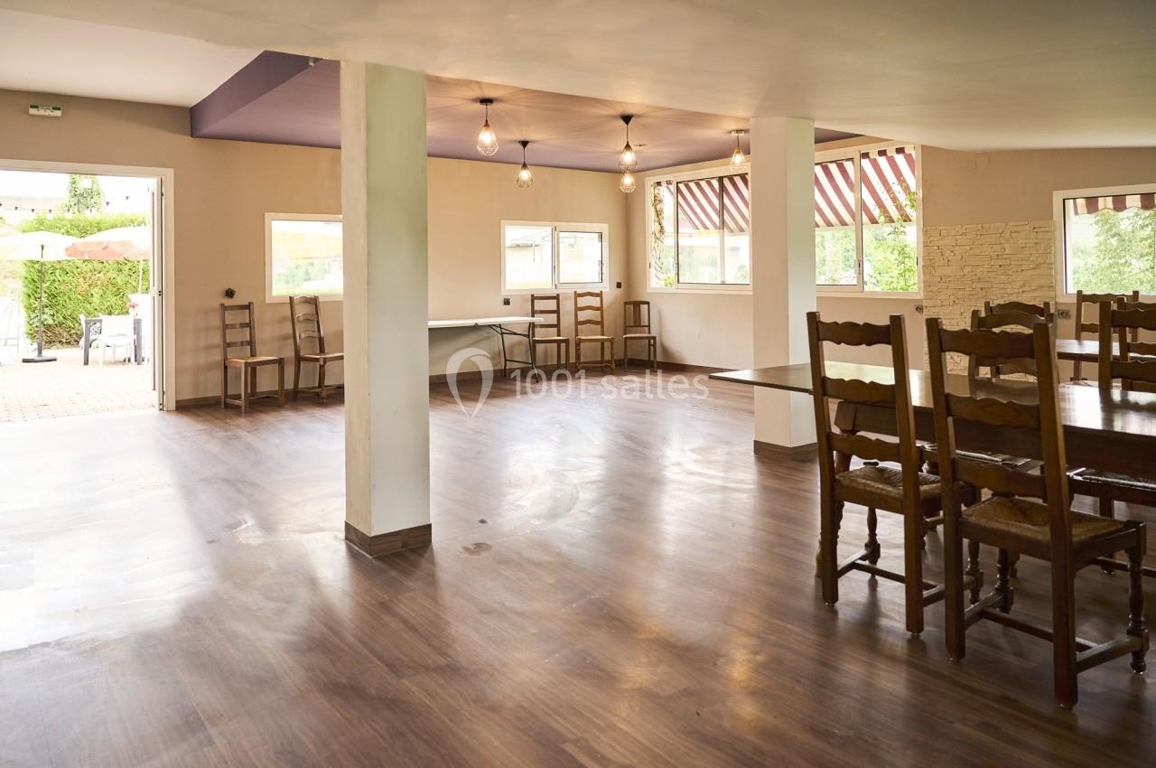 Salle lumineuse avec parquet, grandes fenêtres, chaises en bois et vue sur une terrasse extérieure.