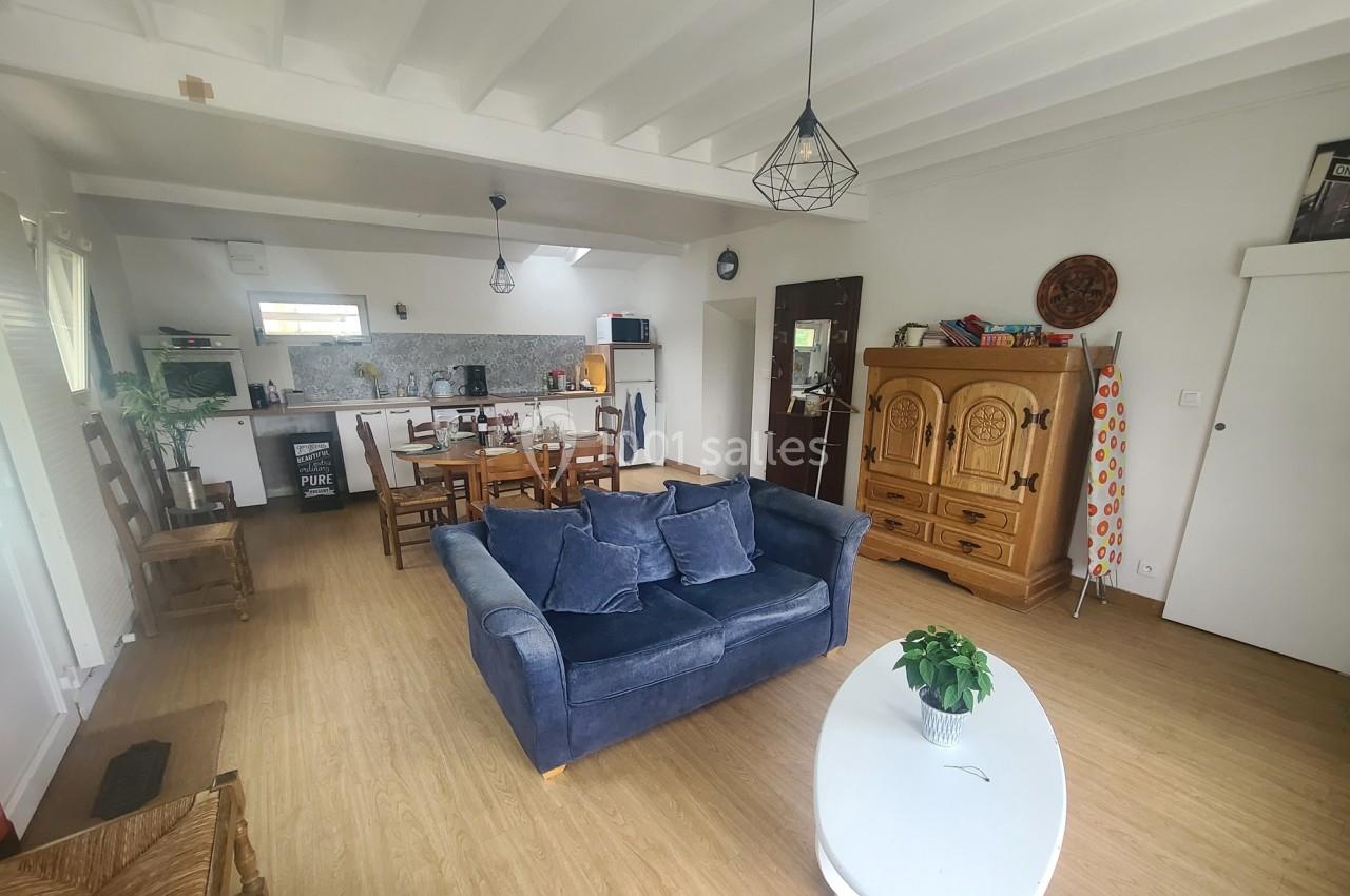 Salon lumineux avec canapé bleu, table à manger en bois, cuisine ouverte et meubles en bois clair.