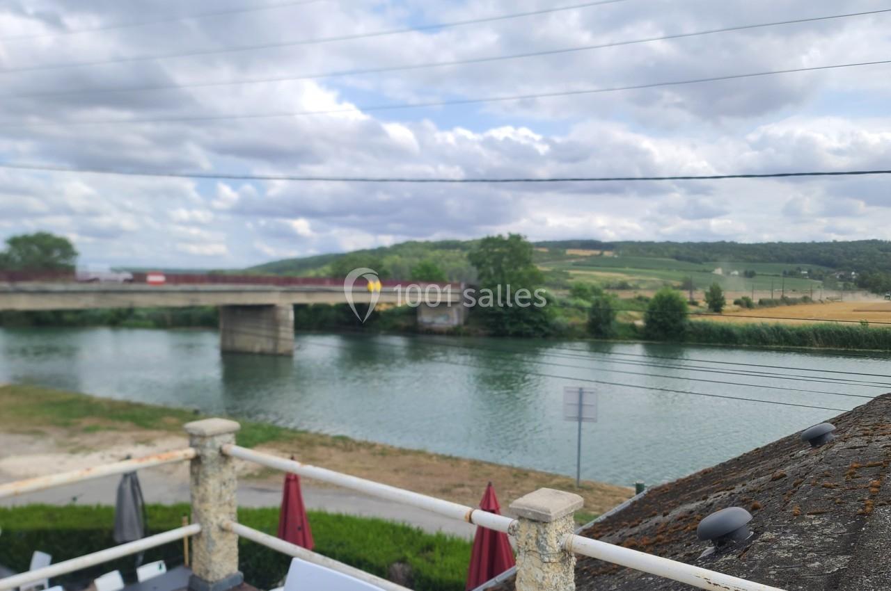 Vue d'un pont traversant une rivière entourée de paysages vallonnés sous un ciel partiellement nuageux.