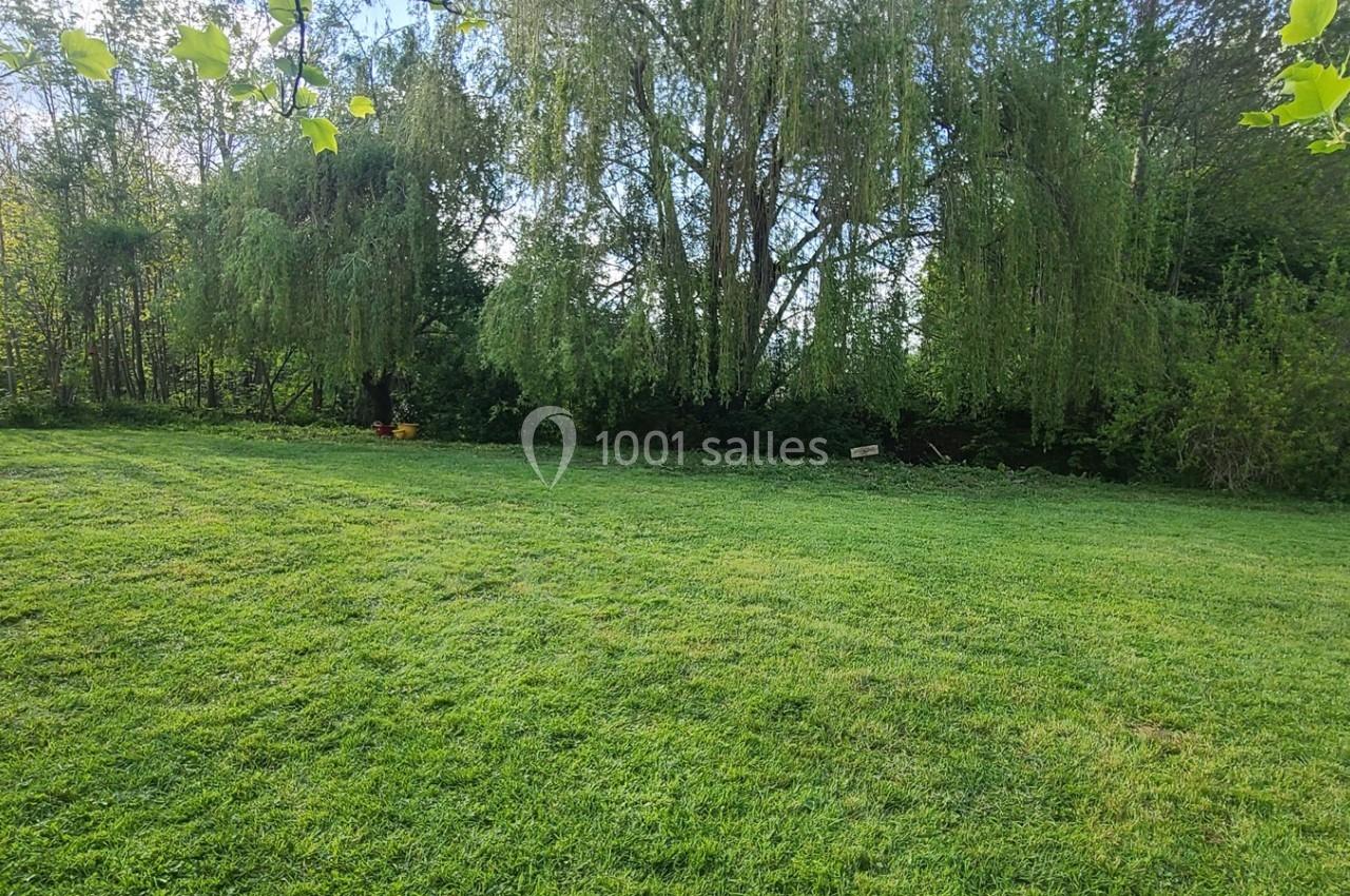 Pelouse verdoyante entourée d'arbres et de buissons sous un ciel dégagé.