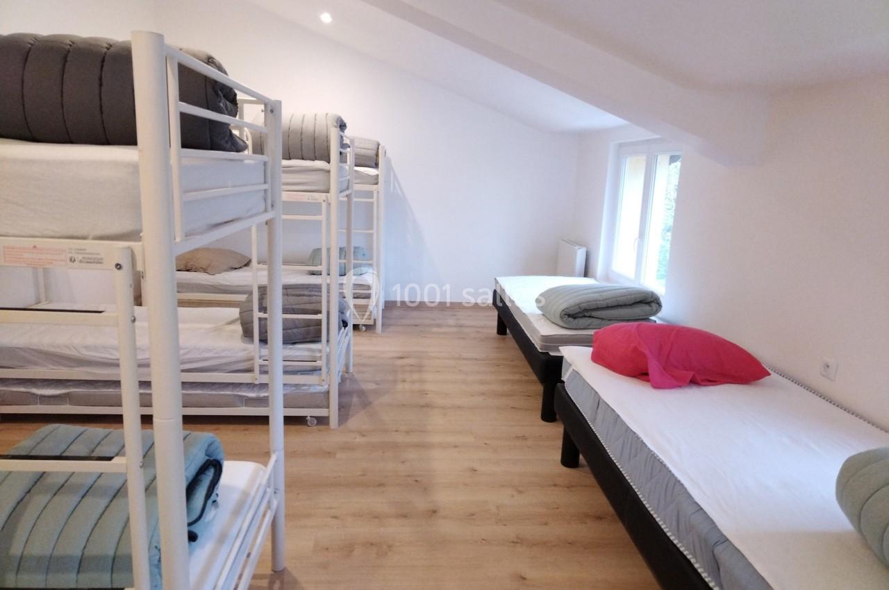 Dortoir avec lits superposés et lits simples, draps pliés sur chaque lit, dans une pièce lumineuse au sol en bois.