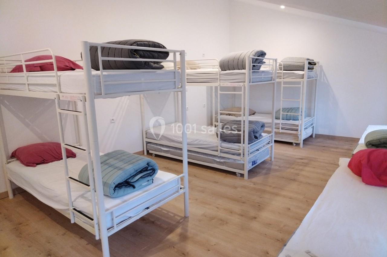 Dortoir avec plusieurs lits superposés équipés de matelas, draps et couvertures dans une pièce lumineuse au sol en bois.