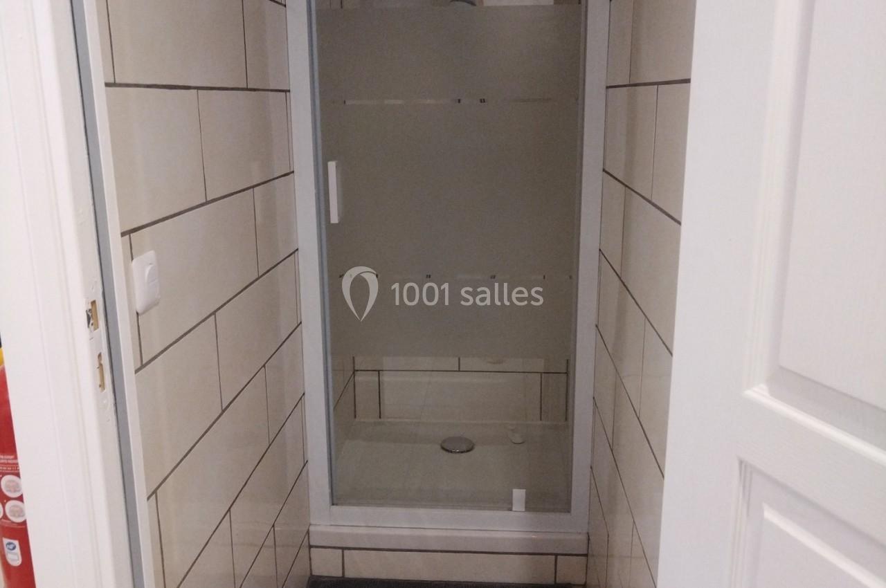 Douche avec porte vitrée opaque dans un espace étroit aux murs carrelés blancs.