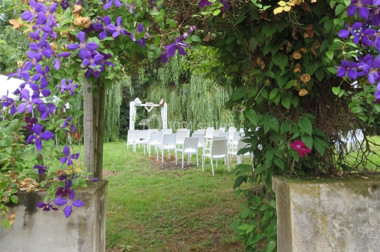 Allée fleurie menant à une cérémonie en plein air avec des chaises blanches et un autel sous un saule pleureur.