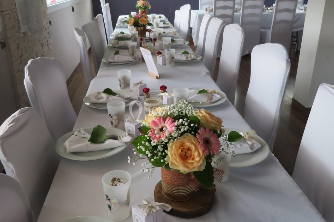 Table dressée pour un événement, décorée avec des fleurs colorées et des couverts disposés sur des nappes blanches.